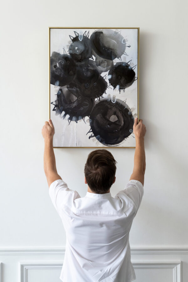 Mann hängt ein Bild mit schwarzen Sonnenblumen an eine weisse Wand